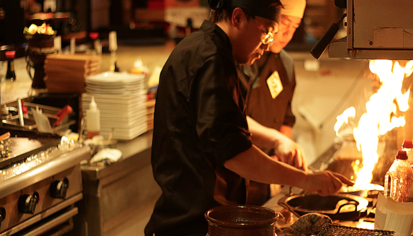 Image of sakebar chefs cooking food over a fire bursting from a grill.