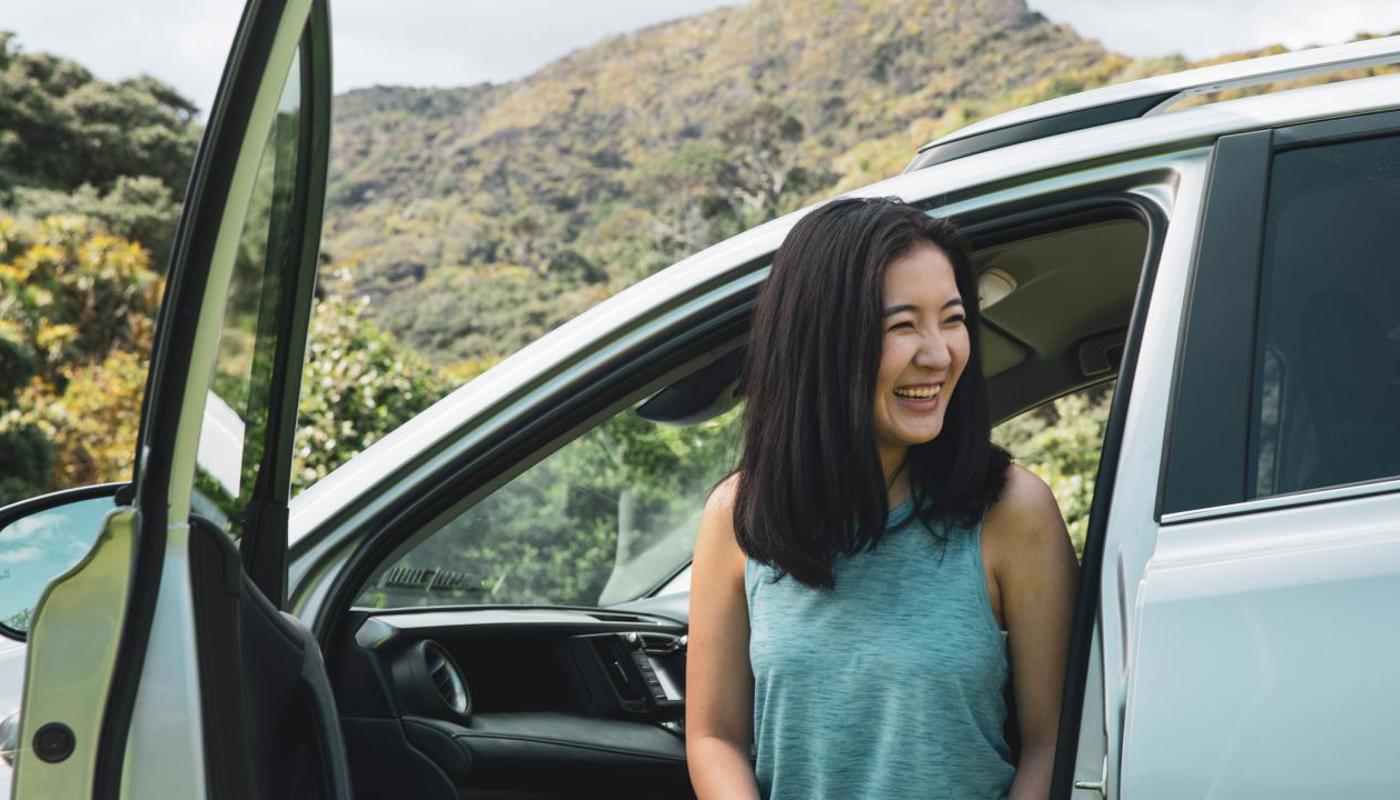 A woman smiling as she exits the passenger side of a GO Rentals car.