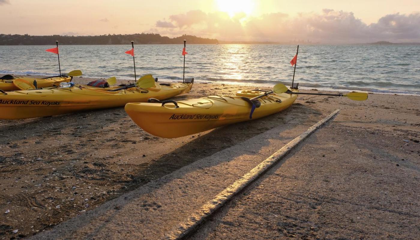 Kayaks on the Beach at Sunset. Going a guided experience with Auckland Sea Kayaks.